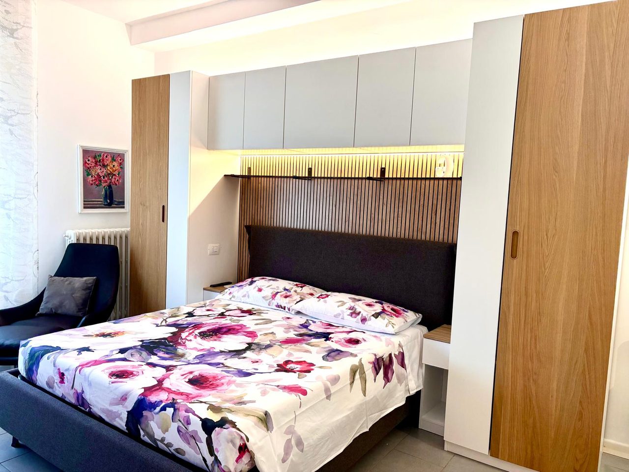 Camera da letto di Mimi's House con armadi su misura, boiserie in legno illuminata e poltrona