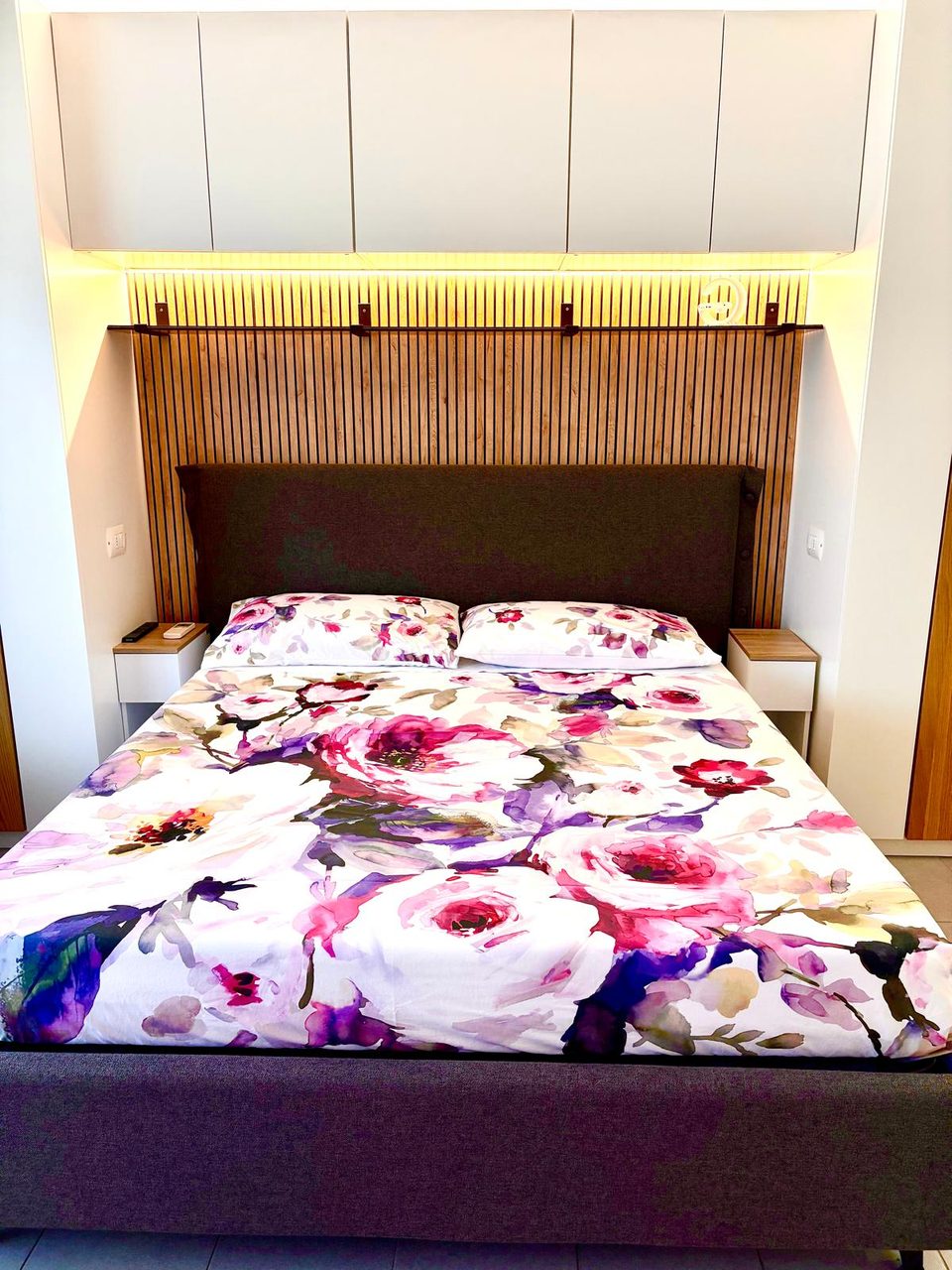 Letto matrimoniale di Mimi's House con testata imbottita, boiserie in legno illuminata e comodini su misura