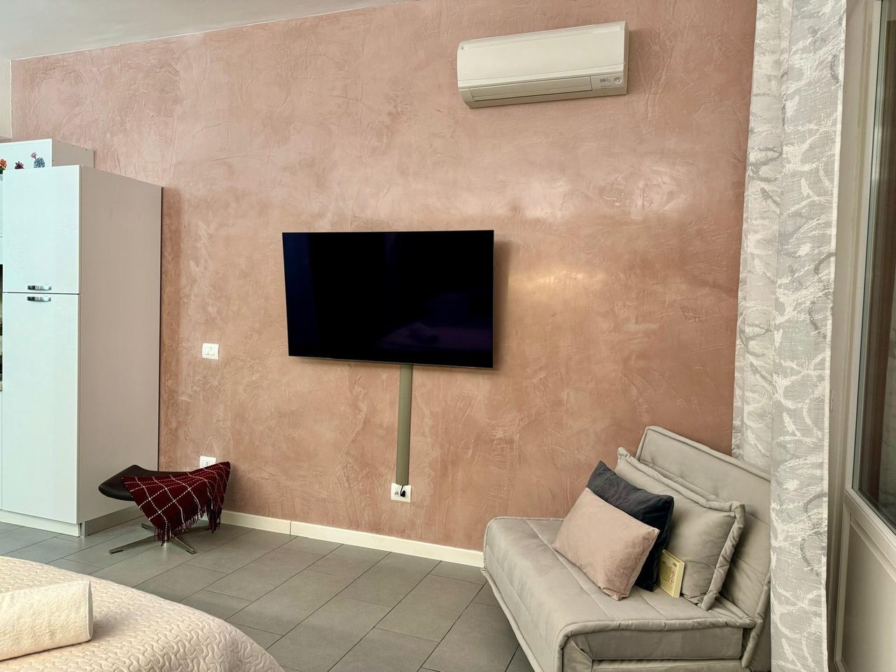 Zona relax di Mimi's House con divano, Smart TV e parete in resina color terracotta